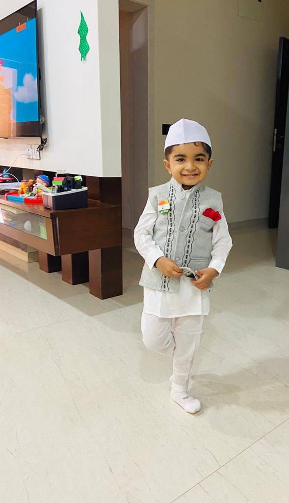 Young Hridan smiling in a white traditional outfit and cap, with a red rose on his waistcoat