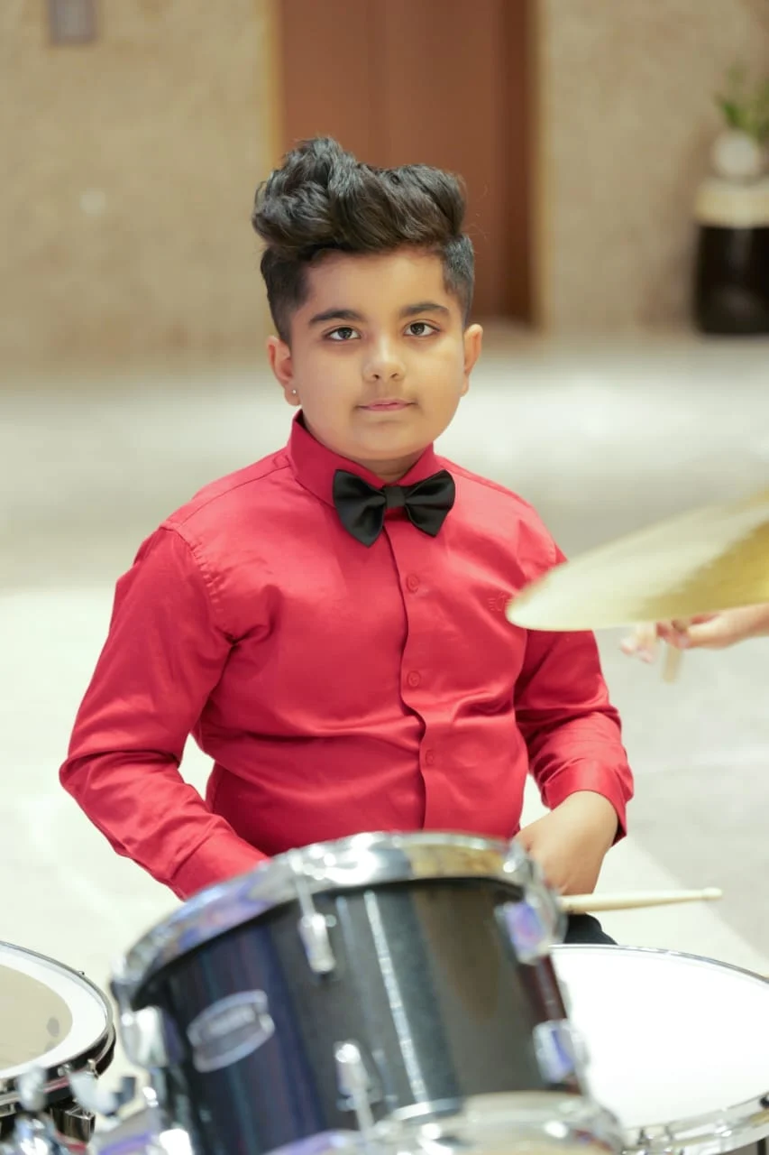 Hridan in a red shirt and bow tie, ready to play the drums